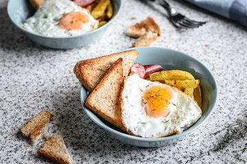 Breakfast with French fries, fried egg, sausage and toast on the table