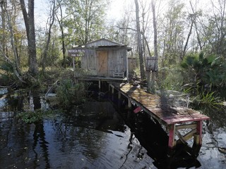 Fototapeta na wymiar small wooden cottage with a dingy and abandoned boat in the swamps of New Orleans, Louisiana