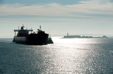 Southampton Water, Hampshire, England, UK. February 2019. Early morning against the light shot of a tug in attendance moving a broad beam oil tanker onto a berth at Fawley refinery.