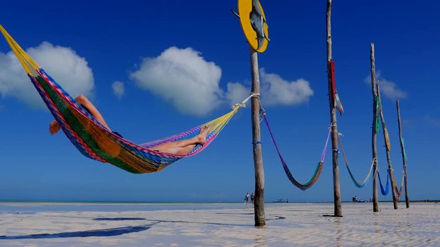 Happy young woman on vacation laying and resting in hammock at sunset in hot summer on Mexico beach