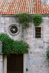 Old european building with red tile round window with wooden door. A shrub grew in a stone wall.