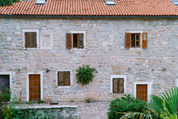 Old european building with red tile round window with wooden door. A shrub grew in a stone wall.
