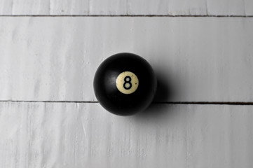 Old billiard ball number 8 black color on white wooden table background, copy space