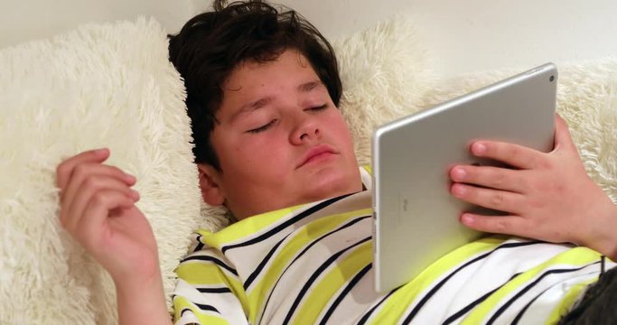 Tired teen lying on sofa with digital tablet at home