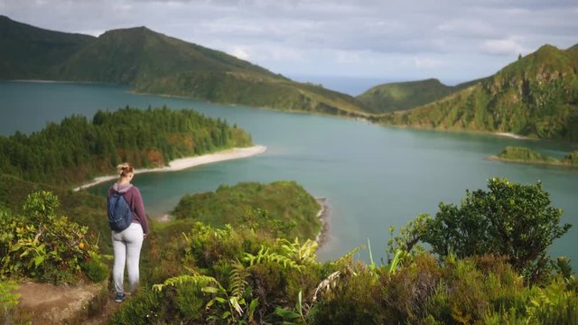 young girl tourist stands near a mountain lake at a height overlooking the ocean