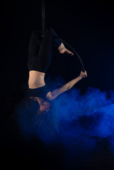 gymnast girl aerial acrobatics on the ring on the background of blue smoke in the dark