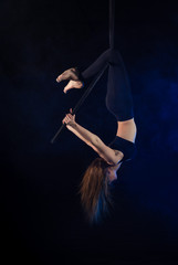 gymnast girl aerial acrobatics on the ring on the background of blue smoke in the dark