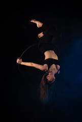 gymnast girl aerial acrobatics on the ring on the background of blue smoke in the dark