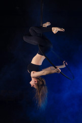 gymnast girl aerial acrobatics on the ring on the background of blue smoke in the dark