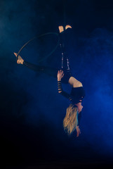 gymnast girl aerial acrobatics on the ring on the background of blue smoke in the dark