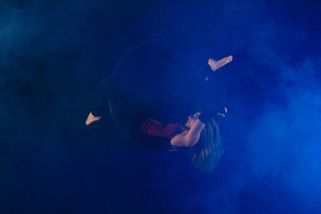 gymnast girl aerial acrobatics on the ring on the background of blue smoke in the dark