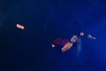 gymnast girl aerial acrobatics on the ring on the background of blue smoke in the dark