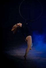 gymnast girl aerial acrobatics on the ring on the background of blue smoke in the dark