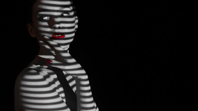 Projection of black and white lines on the girl’s face and body. The face of the girl with an abstract pattern of lines and red lips. Illumination from the blinds in the room. Concept.