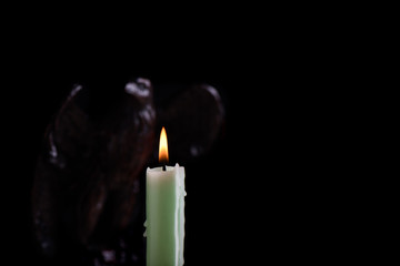 Burning pale green candle illuminates a blurred figure of an eagle, isolated on a black background