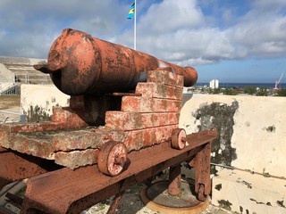 Back view of a cannon at Fort Charlotte with the Nassau harbor in the distance. Also seen is the flag of Nassau. 