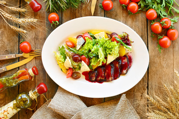 Salad with duck breast, greens, cherry tomatoes, grapes, cheese and oranges on a white plate, isolated on white.