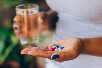 Sick woman holding several medicines in her palm and a glass of water. Taking medicine. Concept of person and self-medication. Health treatment