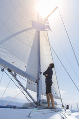  A man on a sailing yacht stands with his back and looks at the open sails.