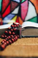 Old red Beads and crucifix on a Bible. Beautiful Stained-glass windows background. Religion concept.