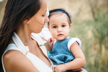 Happy young mother with a small daughter in hands, outdoors background