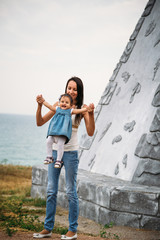 Happy young mother playing with a small daughter, throwing in the air, outdoors background