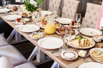 Breakfast table setting arrangement with bread, croissant, cappuccino and orange juice served as the menu. Illuminated with a warm morning light.