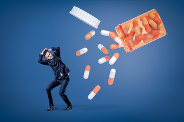 A young man in a suit trying to protect himself from an avalanche of enormous two-colored pills...
