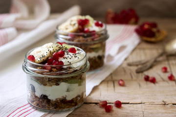 Granola with yogurt and fruit in glass jars on a wooden table. Rustic style.