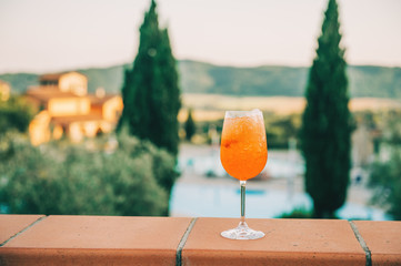 Refreshing aperol spritz cocktails with sliced orange. Tuscany landscape on background