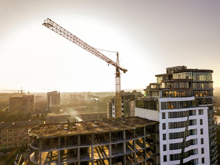 Apartment or office tall building under construction, top view. Tower crane and city landscape stretching to horizon. Drone aerial photography.