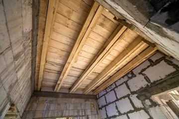 Close-up detail of house room interior under construction and renovation. Energy saving walls of hollow foam insulation blocks, wooden ceiling beams for roof frame.