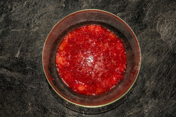 Making of strawberries with sugar on black table in white tile kitchen