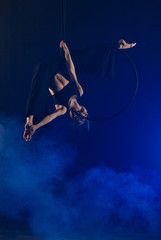 gymnast girl aerial acrobatics on the ring on the background of blue smoke in the dark © Kozlik_mozlik