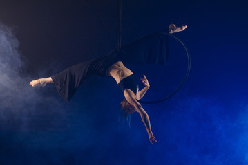 gymnast girl aerial acrobatics on the ring on the background of blue smoke in the dark
