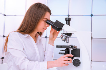 Young woman technician is examining a histological sample, a biopsy in the laboratory of cancer research