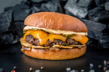 Juicy fresh delicious hamburger. Cheeseburger with beef steak, chedar cheese, pickled cucumbers, tomatoes, onions and sauce on the background of coals. The burger menu.