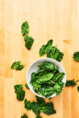 Fresh spinach leaves unwashed in bowl on wooden table. Top view with copy space for text.