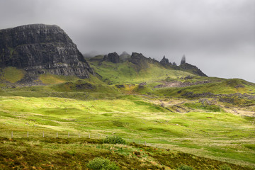 Sun on green pasture before The Old Man of Storr in clouds at The Storr cliff Trotternish peninsula Isle of Skye Scottish Highlands Scotland