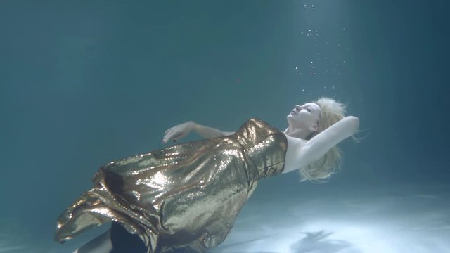 a blonde girl in a beautiful dress swims under water in a water Studio.