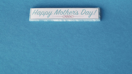 Happy Mothers day written on a small banner laying flat on a blue background with writing space