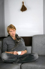 young man in a gray sweater with a Cup of coffee in his hands and his gray cat