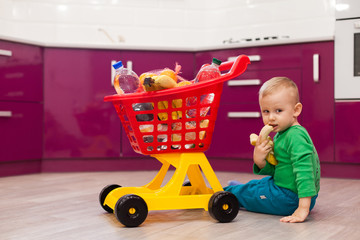 Little boy eats a banana. Cheerful little boy with shopping cart. Little kid in casual wear...