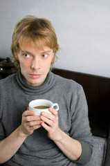young man in a gray sweater with a Cup of coffee in his hands