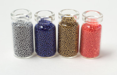 Multicolored beads in glass jars. Beads are poured on a white background. Plastic multi-colored polymers. Plastic pillets.
