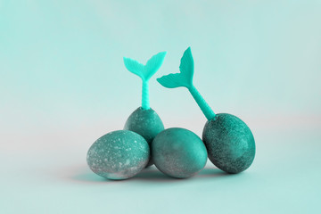 Four cyan color easter eggs lie on a cyan color background. Tails of mermaids stick out of eggs.