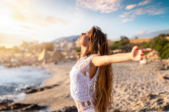 Junge, blonde Frau streckt ihre Arme am Strand aus und genießt die Freiheit und Ruhe