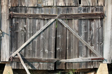 Fototapeta na wymiar Barn wooden doors made of dilapidated wooden boards mounted on wooden wall with rusted metal hinges on concrete foundation on warm sunny day