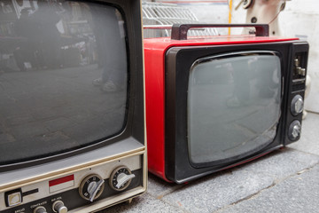 Two vintage televisions for sale on the sidewalk of a weekend flea market