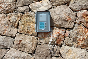 Brand new door entry intercom system mounted on traditional stone wall with hanging electrical...